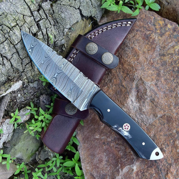 Knife with a damascus blade and leather sheath on a natural stone background